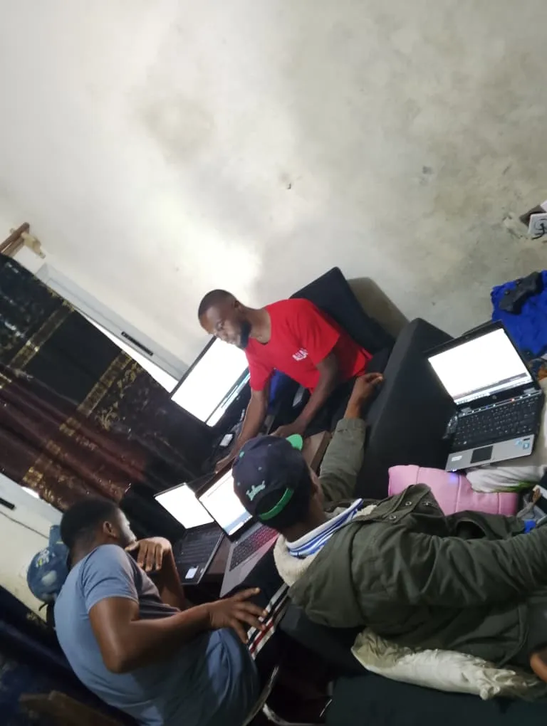A tutor working with a small group of students seated around laptops and notebooks.
