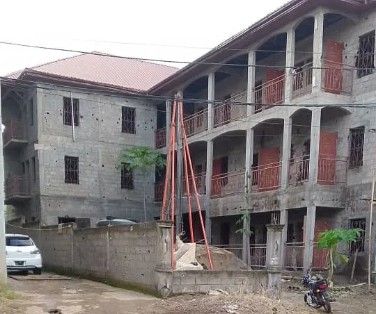 A three-storey reinforced concrete building under construction, its block walls still unrendered and balconies open.