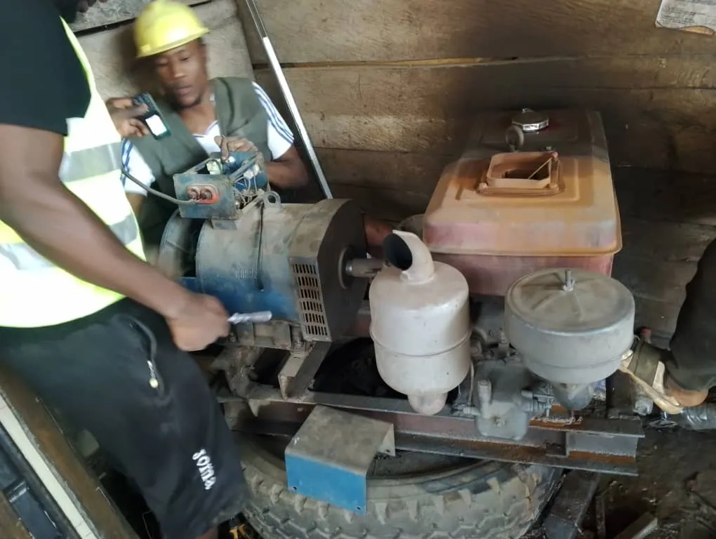 Two technicians in high-visibility vests and a hard hat servicing a diesel generator set in a workshop.