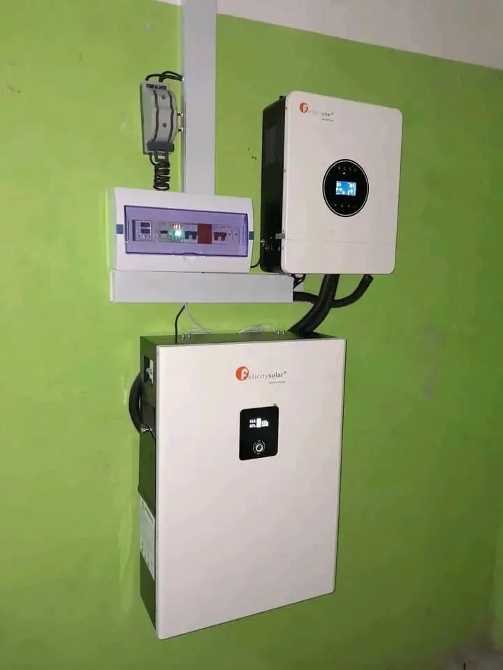 A wall-mounted solar inverter, battery unit and distribution board installed on a green interior wall.