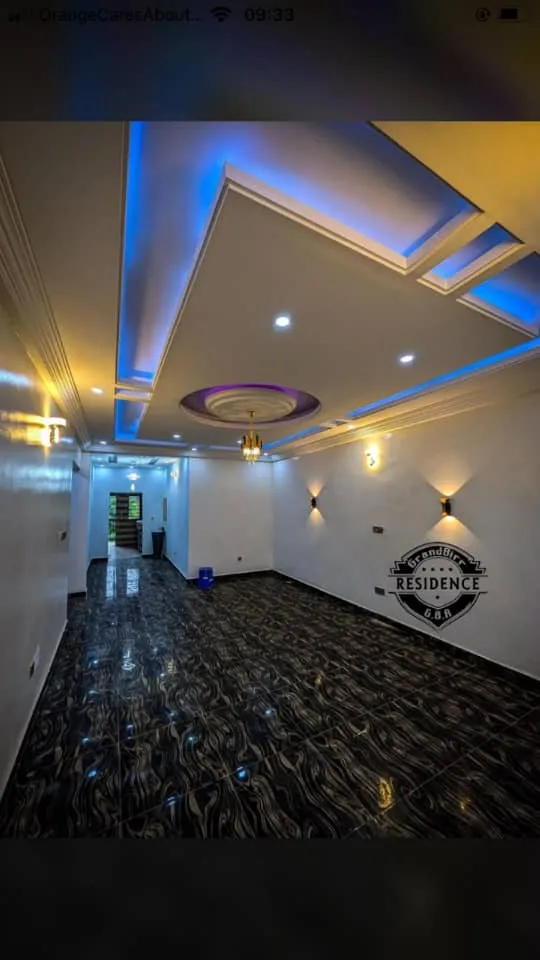 The empty living room of a newly finished home, with polished dark floor tiles and a decorative ceiling lit in blue.